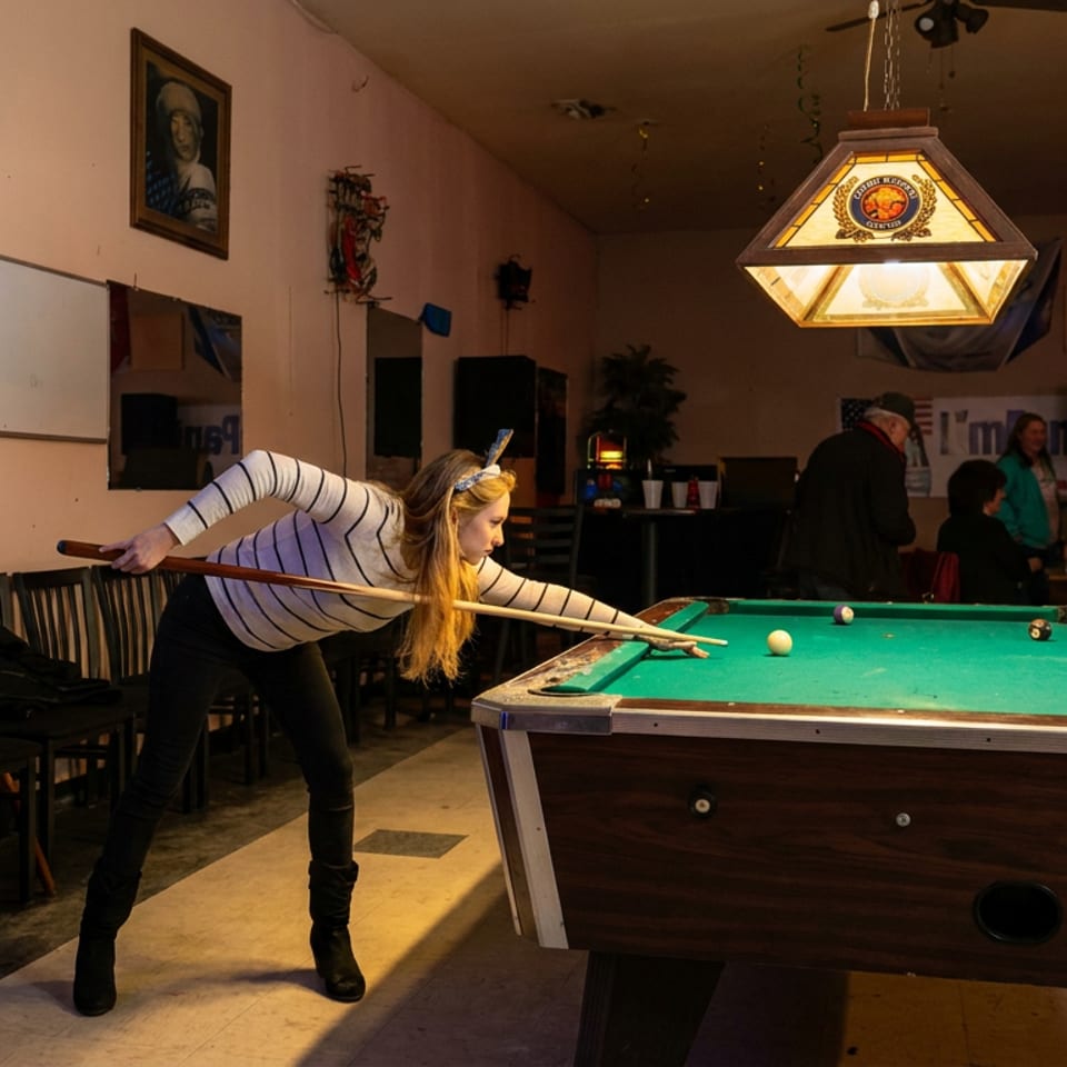 Woman lines up a pool shot in a dimly lit bar with billiards equipment, Bud Light signs, and seated patrons.