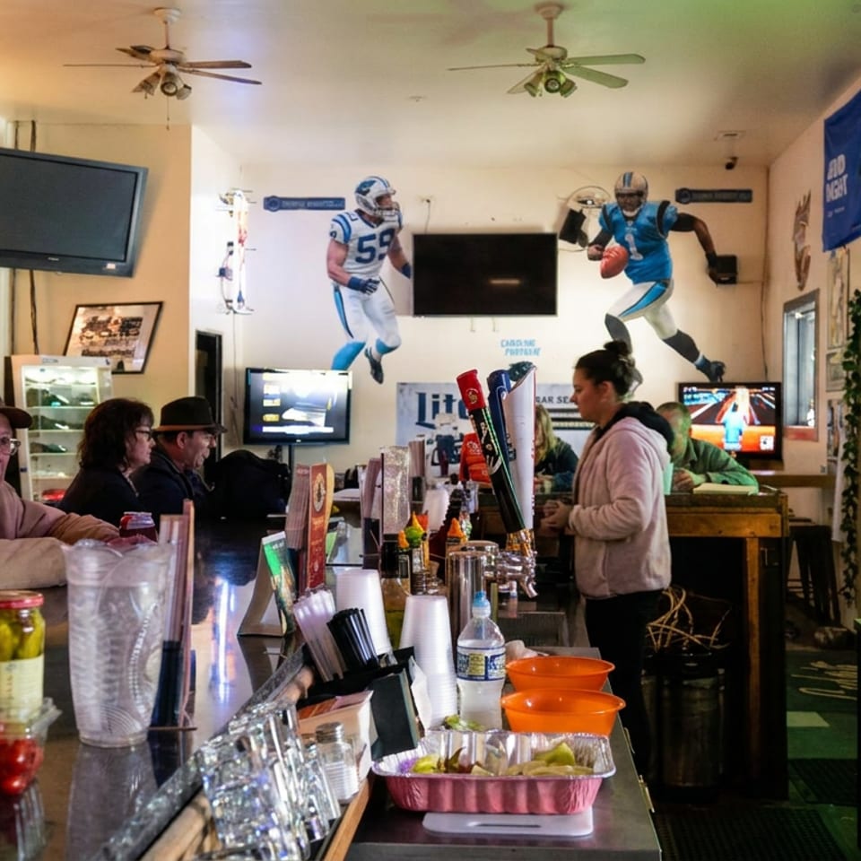 Lively sports bar with patrons at the counter, multiple televisions, football murals, beer taps, and condiment containers.
